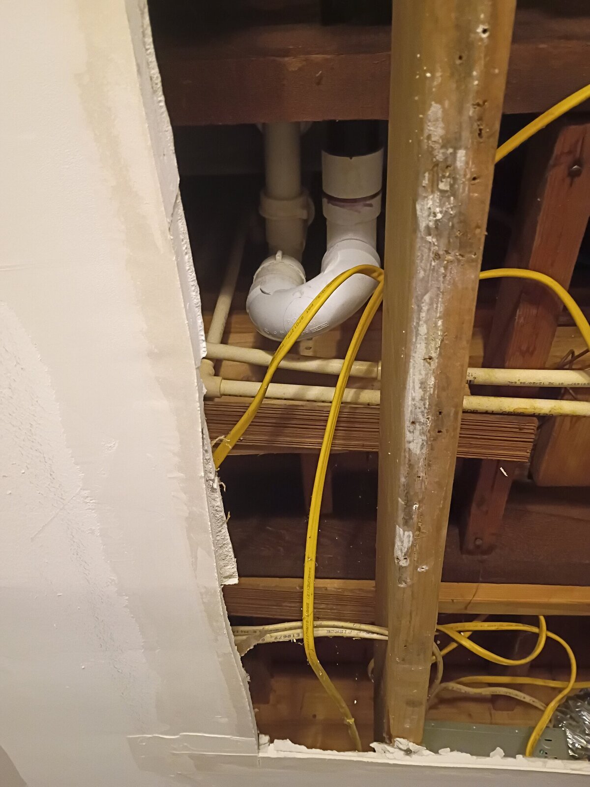 Opened apartment ceiling cavity exposing PVC drain stack, copper supply lines, and framing during leak investigation in Millville, NJ